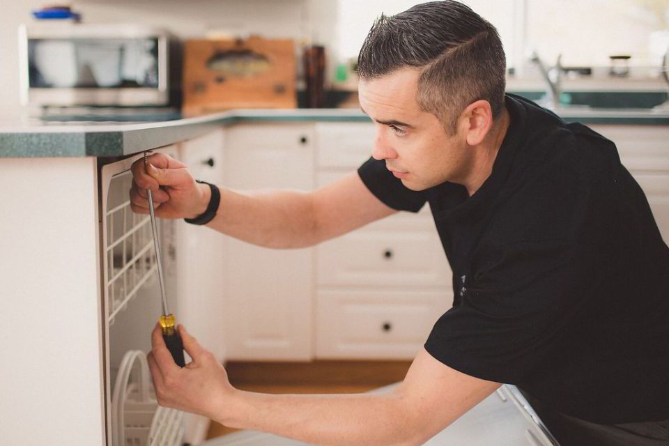 Plumber working on an under-counter appliance in a kitchen